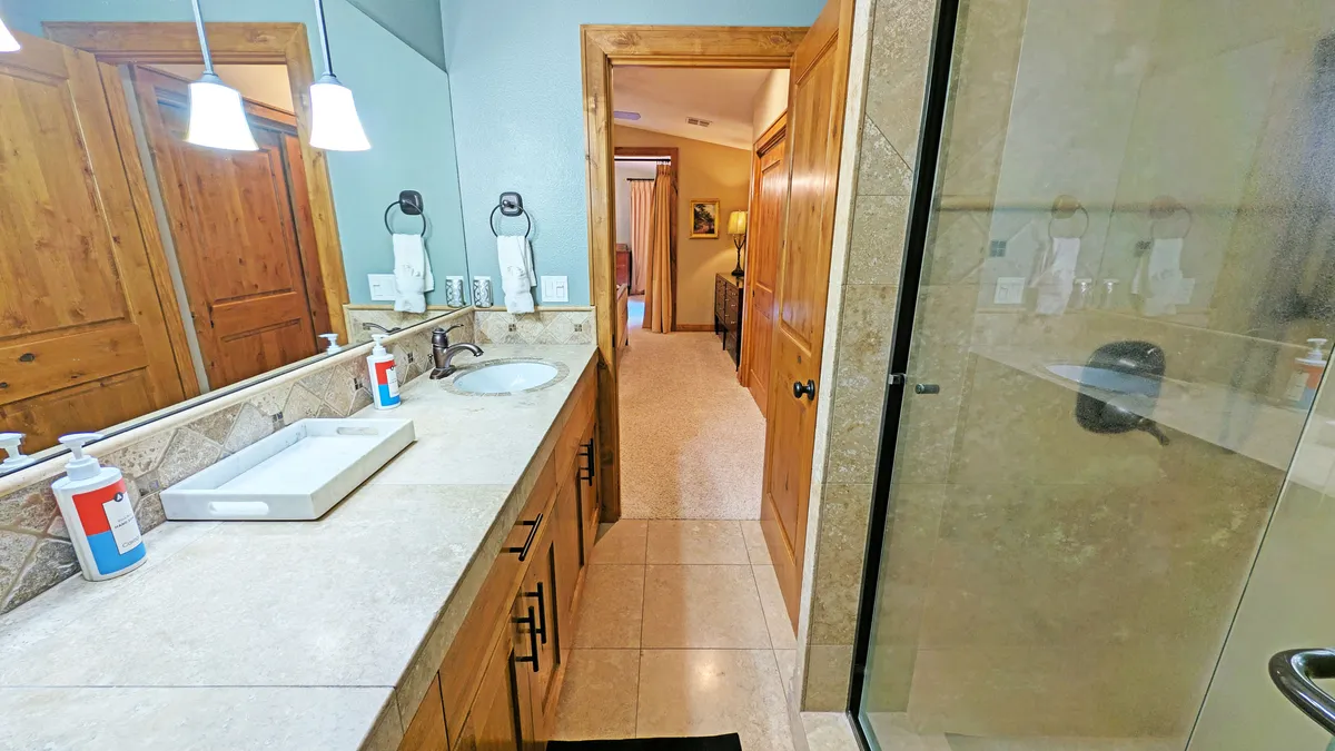 A modern en suite bathroom with a vanity sink, a spacious glass-enclosed shower area, a mirror, and wooden cabinetry. The design is clean and calming, perfect for a rejuvenating shower.