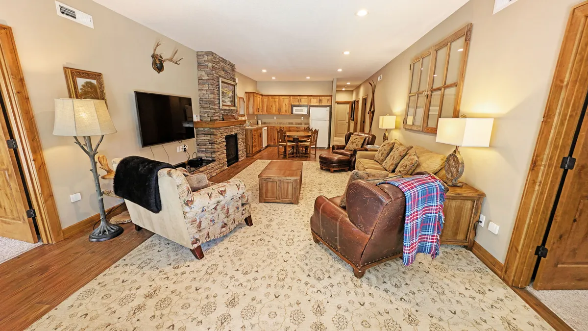 A cozy interior living space is shown with a large stone fireplace, wooden cabinets, comfortable seating, and a large television—ideal for movie nights or relaxing after a day of adventure.