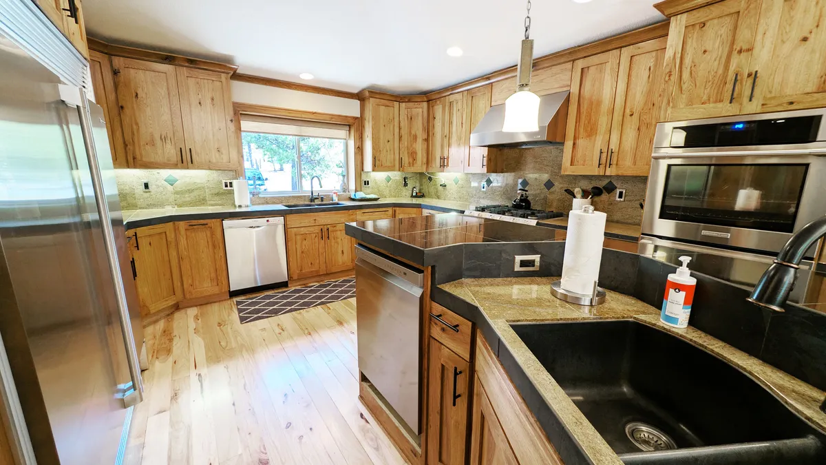 A beautifully appointed kitchen featuring granite countertops, premium stainless steel appliances—including double ovens and a Sub-Zero refrigerator—wooden cabinetry, and a sunlit window above the double sink. The space is both highly functional and visually appealing, catering to both chefs and casual cooks.