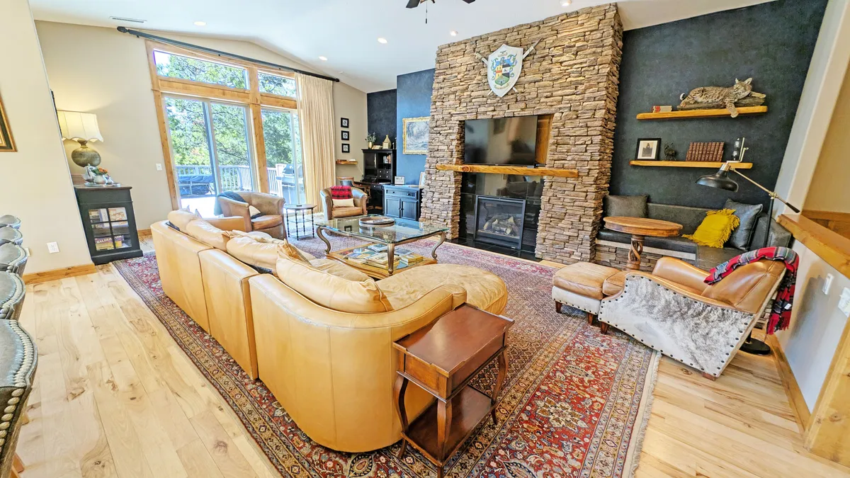 The hero image showcases a spacious, inviting living area with a stunning floor-to-ceiling stone fireplace as the centerpiece. Plush, comfortable seating surrounds the fireplace, while large windows let in abundant natural light and offer views of the outdoors. Decorative wall art adds a touch of warmth and personality, creating a cozy setting ideal for family gatherings or relaxing evenings.