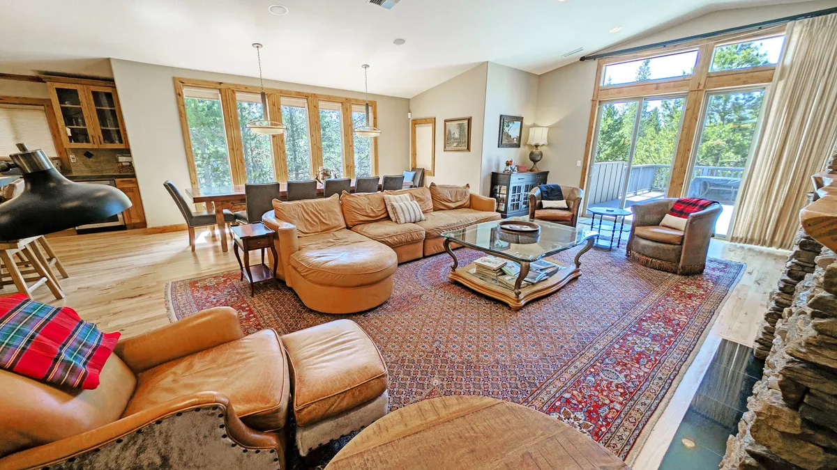 A cozy, sunlit living area featuring a comfortable seating arrangement, large windows, a central coffee table, and wooden accents. The space is perfect for social gatherings, family game nights, and relaxing together after a day of activities.