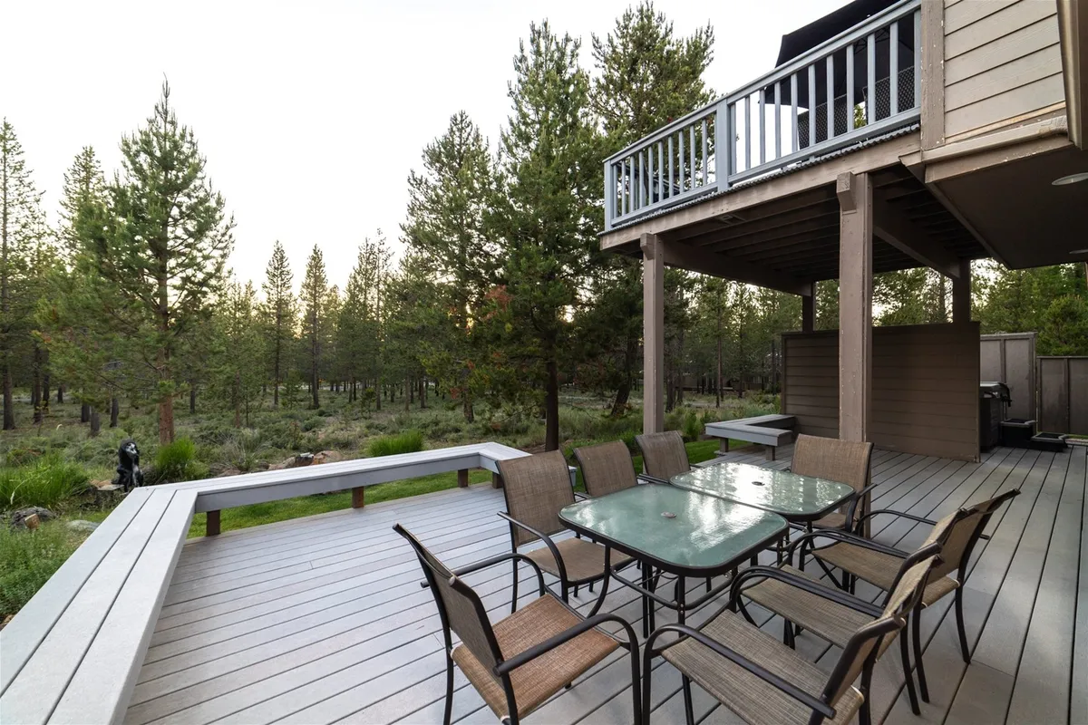 This image displays a deck area surrounded by trees, featuring an outdoor dining table, inviting guests to gather and enjoy meals in nature. The tranquil, scenic backdrop highlights the beauty of the Sunriver landscape and the potential for sunset views or stargazing at night.