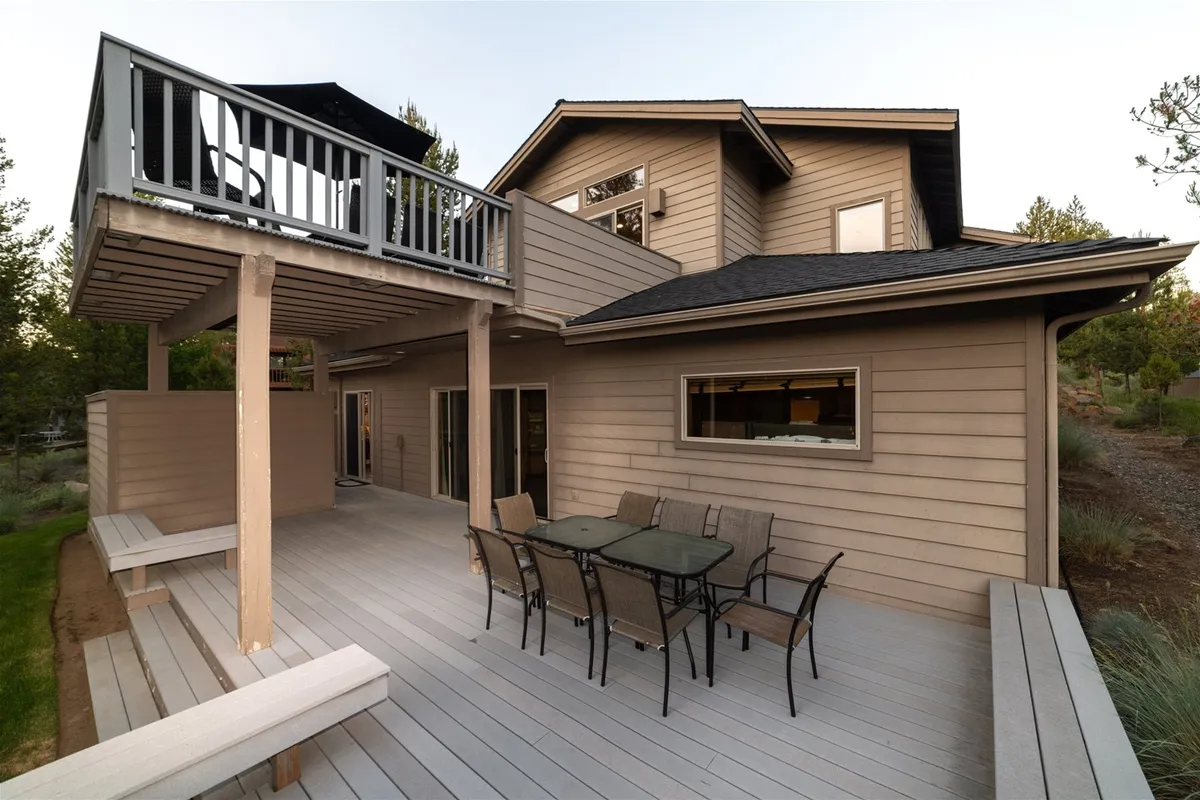 This exterior view captures a multi-level deck with a dining table and an upper balcony set amidst lush greenery. The space is clearly designed for outdoor dining and relaxation, with ample room for social gatherings or quiet moments taking in the views.