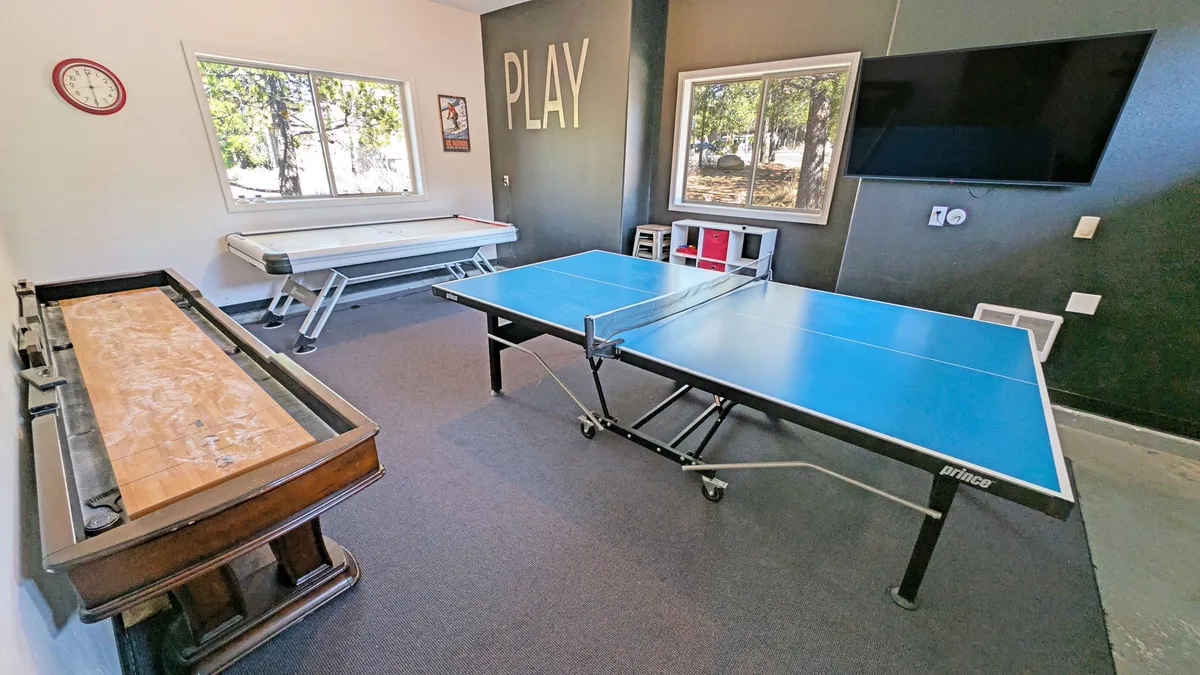 This energetic interior photo showcases a spacious game room complete with a ping pong table, air hockey table, a large window with natural light, and a playful 'PLAY' sign on the wall. The space is open, inviting, and filled with activity, making it an ideal spot for families to gather and have fun.