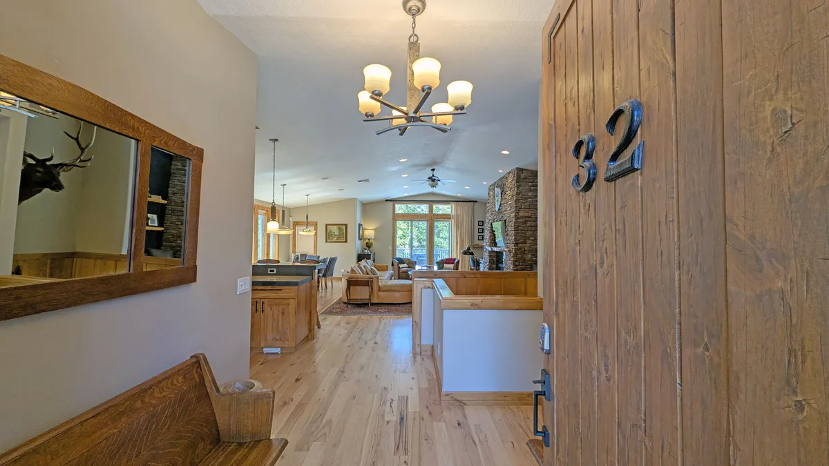 A welcoming entryway is depicted, featuring a sturdy front door with the number 32, a wooden bench, a decorative mirror, and a tasteful chandelier. The space exudes hospitality and functionality, echoing the sense of arrival and organization.