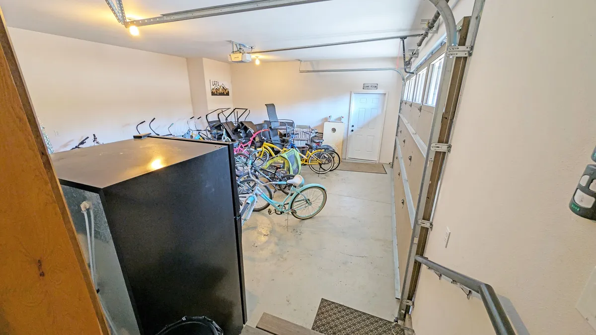 A practical garage space showcases multiple bicycles, a refrigerator, and convenient storage options with a view of the garage door. The arrangement emphasizes the utility and readiness for group activities or transitions.