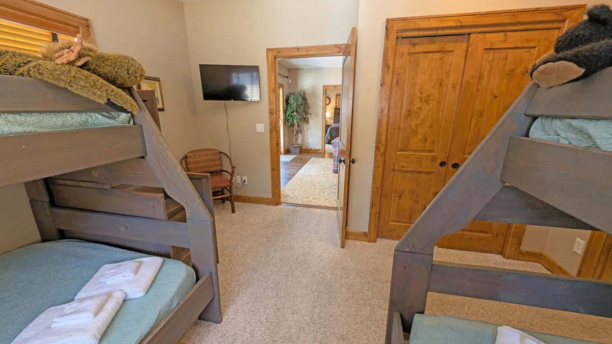 A family-friendly bunk room featuring two sets of wooden bunk beds, a closet, a television, and a doorway leading to another room. The room is bright and welcoming, designed for kids or teens to feel at home.