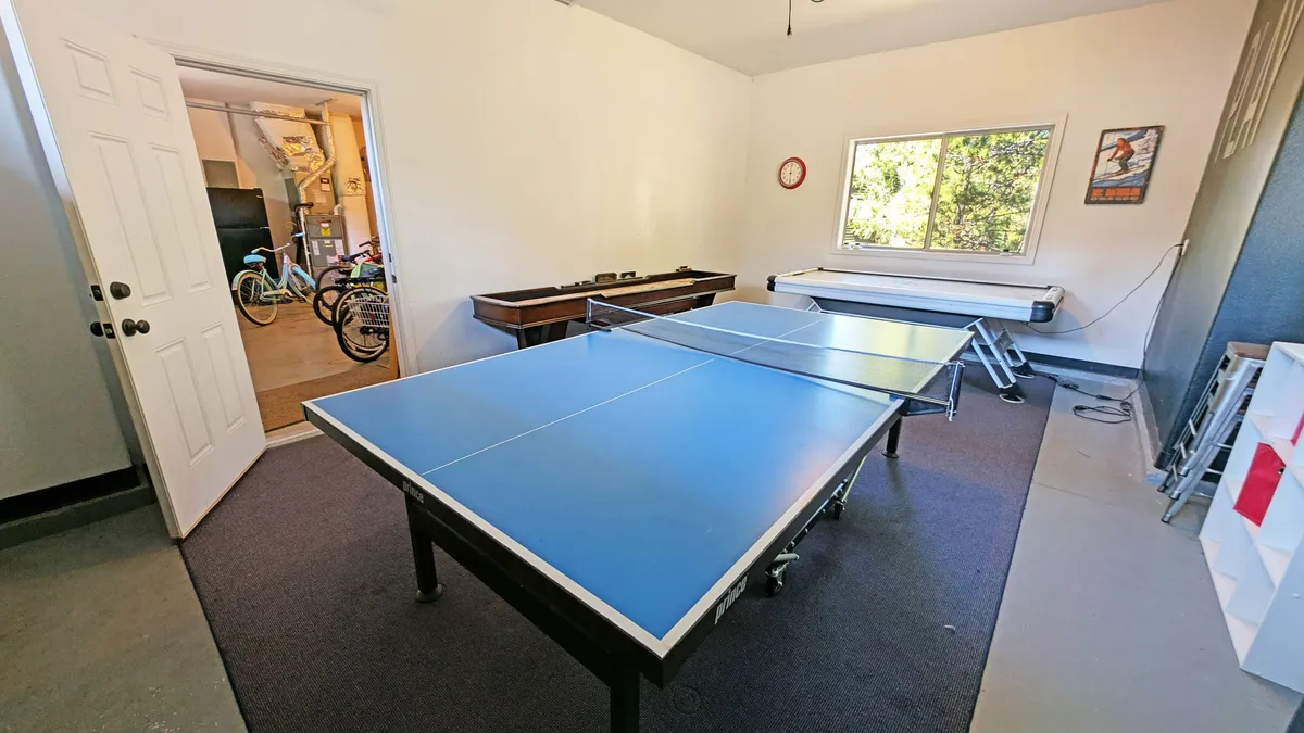 A lively game room featuring ping pong tables, a window letting in natural light, and bicycles visible in the background. The room exudes energy and encourages friendly competitions and group activities.